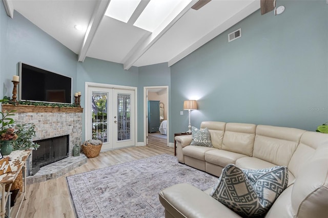 living room featuring vaulted ceiling with beams, light wood-type flooring, a fireplace, and french doors