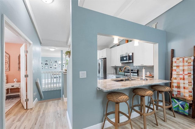 kitchen with white cabinets, appliances with stainless steel finishes, backsplash, light wood-type flooring, and light stone counters