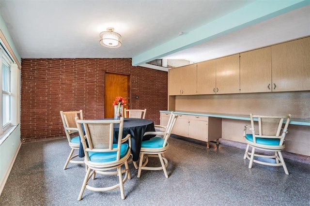 dining space featuring brick wall and vaulted ceiling with beams