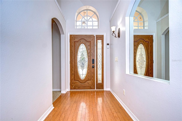 foyer entrance featuring crown molding, light hardwood / wood-style floors, and a towering ceiling