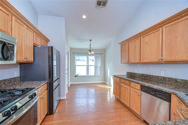 kitchen featuring lofted ceiling, appliances with stainless steel finishes, dark stone countertops, decorative light fixtures, and light wood-type flooring