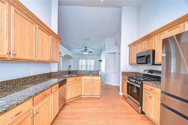 kitchen featuring sink, ceiling fan, appliances with stainless steel finishes, dark stone counters, and light wood-type flooring