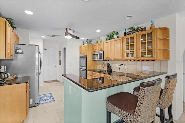 kitchen featuring a peninsula, a kitchen breakfast bar, appliances with stainless steel finishes, decorative backsplash, and glass insert cabinets