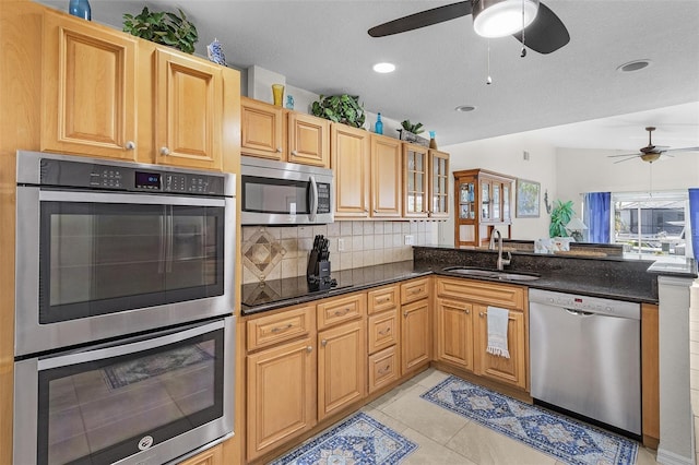 kitchen with light tile patterned flooring, stainless steel appliances, a peninsula, a sink, and backsplash