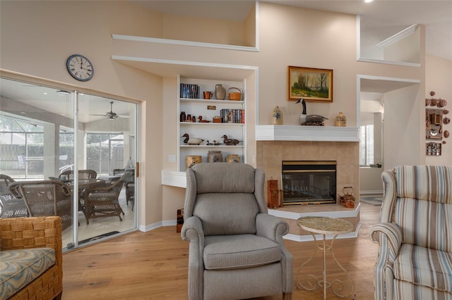 living room featuring a tiled fireplace, ceiling fan, and light wood-type flooring