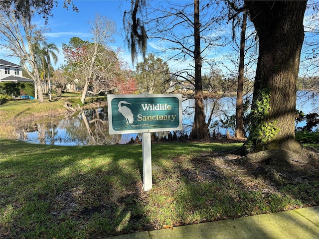 community sign with a water view and a yard