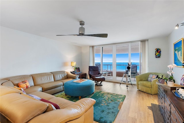 living room with floor to ceiling windows, a water view, light hardwood / wood-style flooring, and ceiling fan