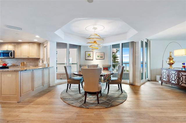 dining space featuring sink, a tray ceiling, a chandelier, and light hardwood / wood-style floors