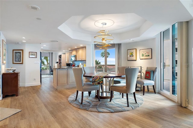 dining area with a raised ceiling, a healthy amount of sunlight, an inviting chandelier, and light hardwood / wood-style flooring