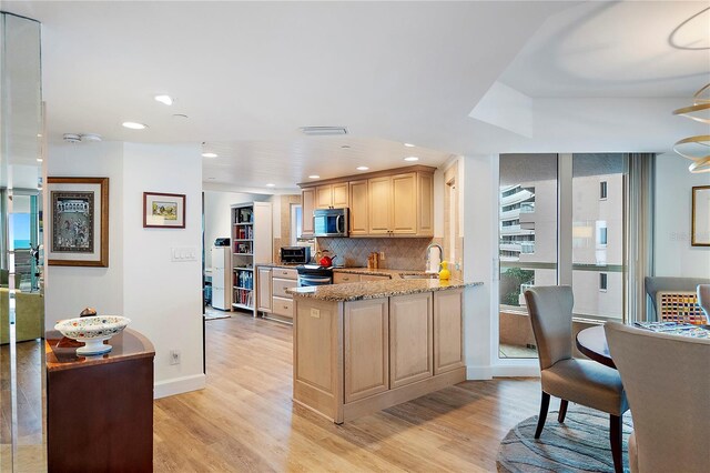 kitchen featuring light hardwood / wood-style floors, kitchen peninsula, decorative backsplash, light brown cabinets, and light stone counters