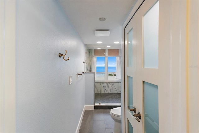 bathroom featuring tile patterned floors, toilet, tiled shower, and a water view