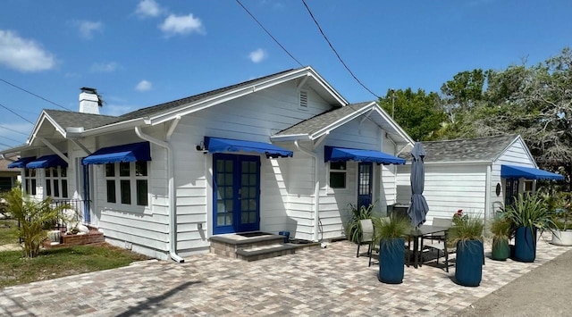 back of property featuring a patio, roof with shingles, and a chimney