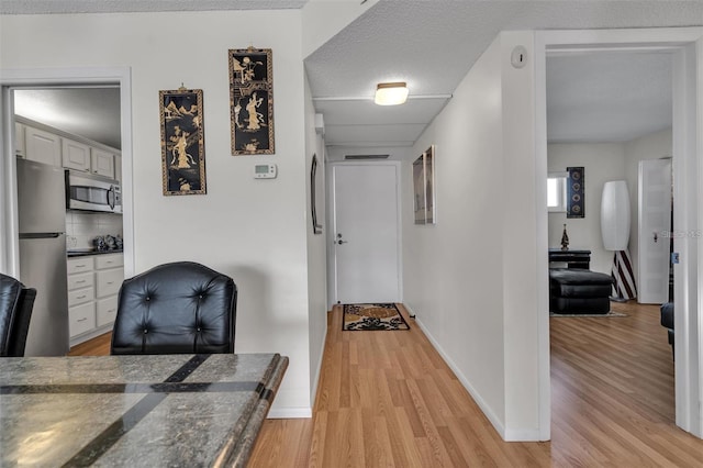 corridor with a textured ceiling and light hardwood / wood-style flooring