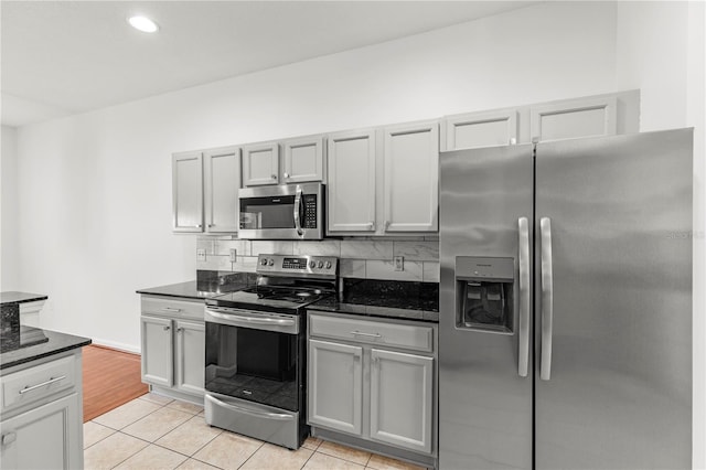 kitchen with light tile patterned floors, appliances with stainless steel finishes, dark stone counters, and gray cabinets