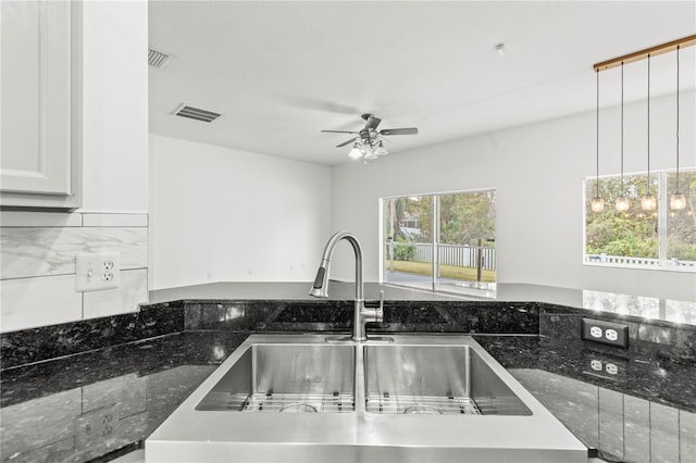 kitchen featuring ceiling fan, dark stone countertops, pendant lighting, sink, and white cabinetry