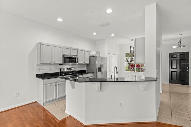 kitchen with a kitchen bar, stainless steel appliances, decorative backsplash, kitchen peninsula, and light tile patterned floors