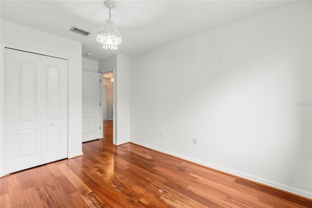 unfurnished bedroom featuring hardwood / wood-style floors, a closet, and a notable chandelier