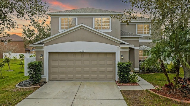 traditional-style house featuring roof with shingles, stucco siding, concrete driveway, a lawn, and an attached garage