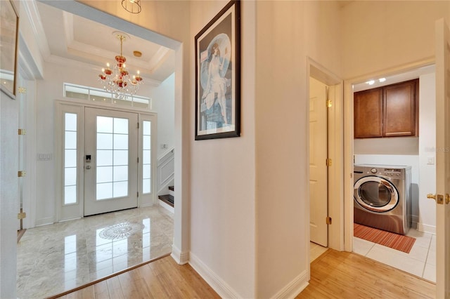 foyer entrance with an inviting chandelier, a tray ceiling, washer / dryer, and light hardwood / wood-style flooring