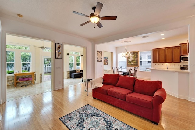 living room featuring ceiling fan with notable chandelier and light wood-type flooring