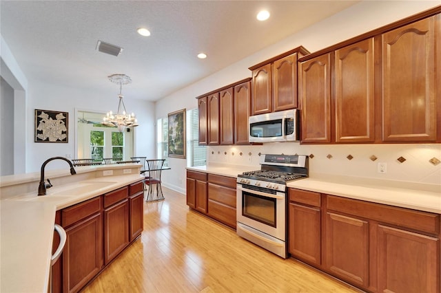 kitchen with decorative backsplash, hanging light fixtures, a notable chandelier, light hardwood / wood-style floors, and stainless steel appliances