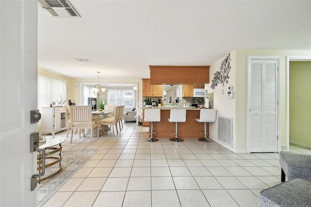 kitchen featuring a kitchen bar, tasteful backsplash, light tile patterned floors, kitchen peninsula, and pendant lighting