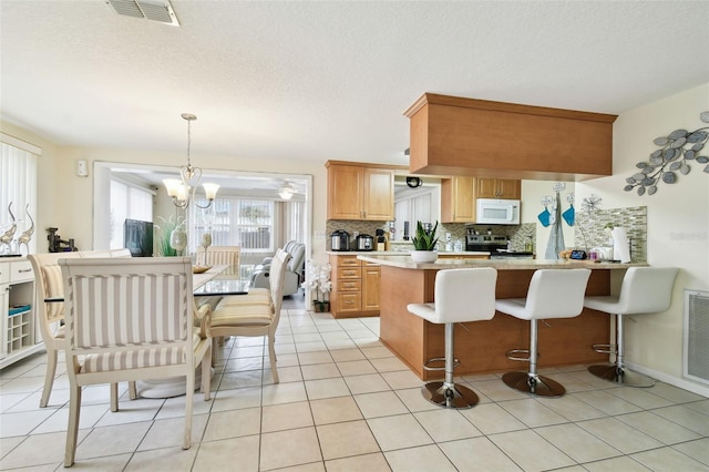 kitchen featuring backsplash, stainless steel range with electric stovetop, hanging light fixtures, light tile patterned floors, and an inviting chandelier