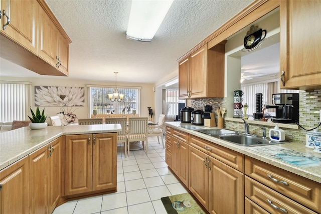 kitchen featuring sink, decorative light fixtures, light tile patterned floors, ceiling fan with notable chandelier, and backsplash