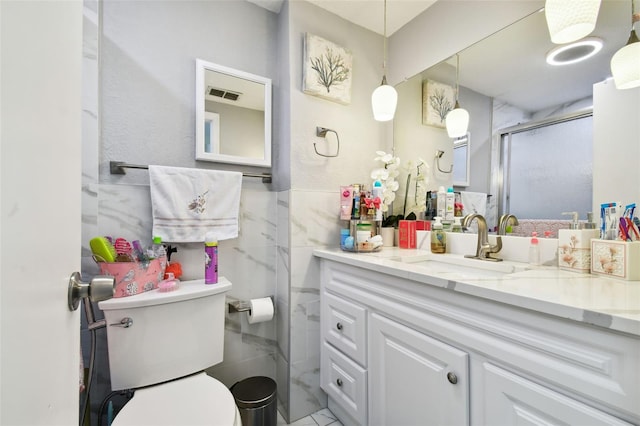 bathroom featuring vanity, toilet, a shower with shower door, and tile walls