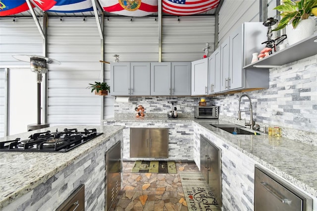 kitchen with light stone counters, gray cabinets, black gas stovetop, and sink