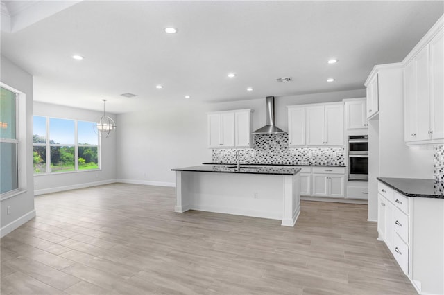 kitchen with white cabinetry, wall chimney range hood, tasteful backsplash, and sink