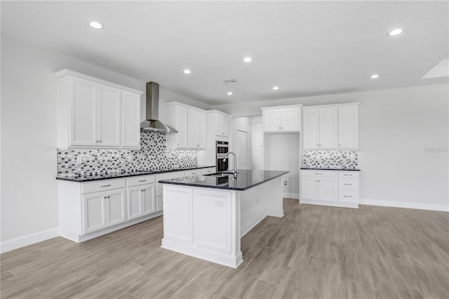 kitchen with a kitchen island with sink, white cabinetry, wall chimney exhaust hood, and light wood-type flooring