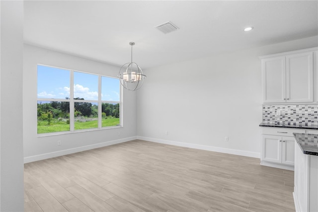 unfurnished dining area with a chandelier and light wood-type flooring