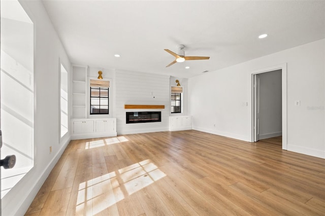 unfurnished living room featuring ceiling fan, a large fireplace, light hardwood / wood-style floors, and built in features