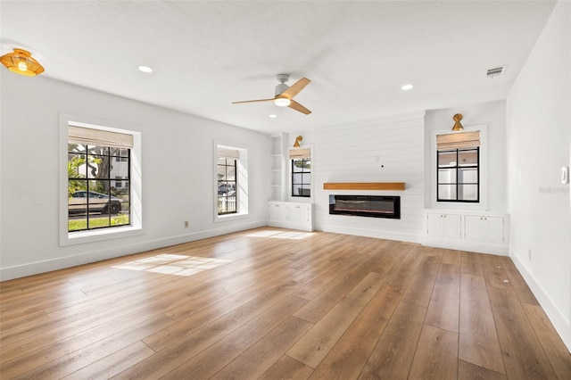 unfurnished living room with ceiling fan, a large fireplace, built in features, and light hardwood / wood-style flooring