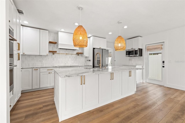 kitchen with pendant lighting, a center island with sink, white cabinets, and appliances with stainless steel finishes