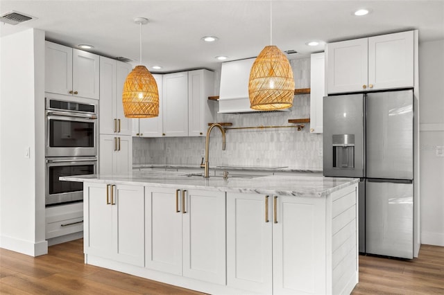 kitchen with appliances with stainless steel finishes, a kitchen island with sink, hardwood / wood-style floors, light stone counters, and white cabinets