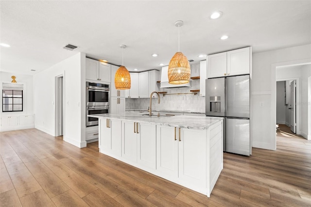 kitchen with a kitchen island with sink, light stone countertops, white cabinets, and appliances with stainless steel finishes