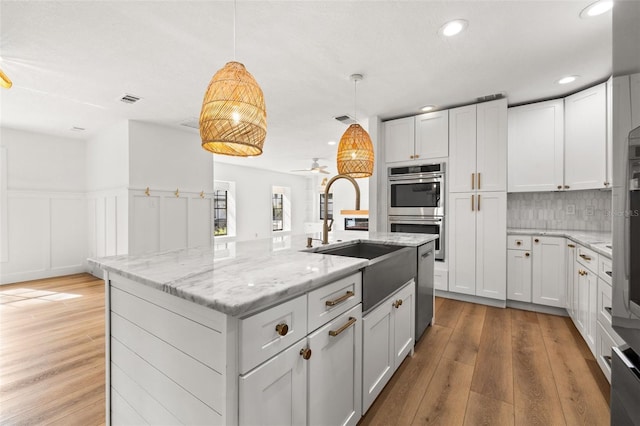 kitchen featuring double oven, decorative light fixtures, sink, white cabinets, and a kitchen island with sink