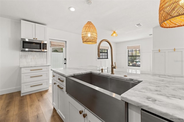 kitchen featuring white cabinetry, sink, light stone counters, and pendant lighting