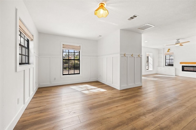 unfurnished living room featuring ceiling fan, a fireplace, light hardwood / wood-style flooring, and a textured ceiling