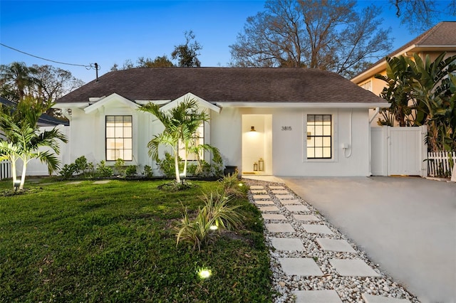 view of front of property with stucco siding, a shingled roof, a front yard, a gate, and fence