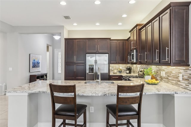 kitchen with sink, backsplash, a kitchen breakfast bar, stainless steel appliances, and light stone countertops