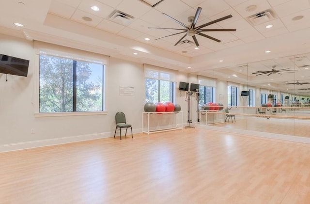 exercise area featuring ceiling fan, light wood-type flooring, and a tray ceiling