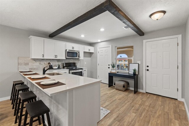 kitchen with tasteful backsplash, a kitchen bar, sink, appliances with stainless steel finishes, and white cabinets