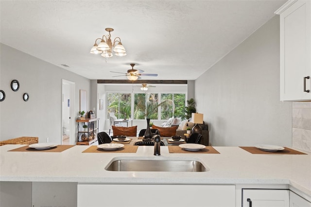 kitchen with ceiling fan with notable chandelier, sink, and white cabinetry