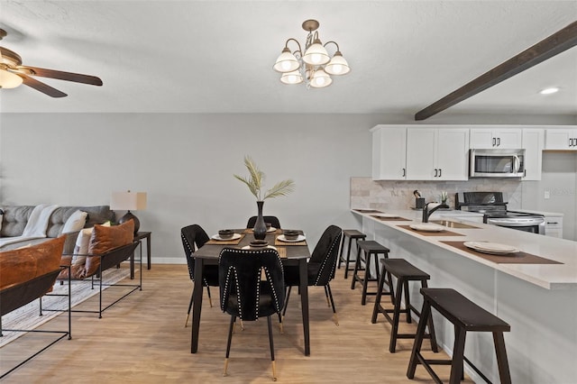 dining area with beam ceiling, sink, ceiling fan with notable chandelier, and light hardwood / wood-style floors