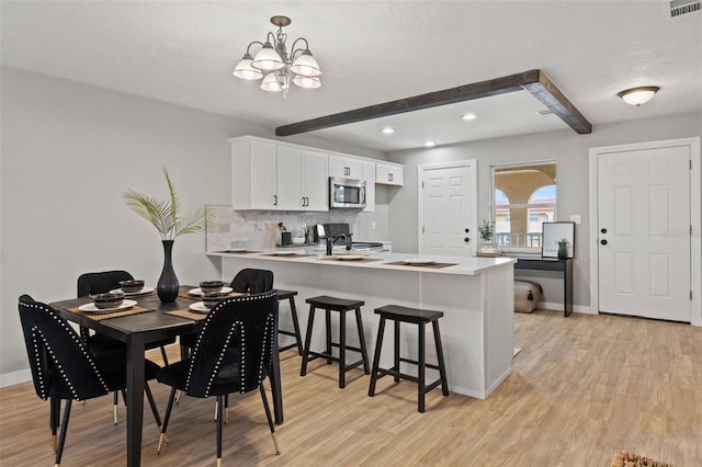 dining space featuring beam ceiling, a notable chandelier, and light hardwood / wood-style floors