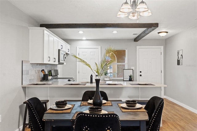 dining area featuring light wood-type flooring, beamed ceiling, and an inviting chandelier