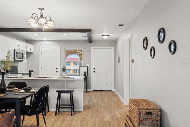 kitchen featuring white cabinetry, kitchen peninsula, a breakfast bar, light hardwood / wood-style flooring, and beam ceiling